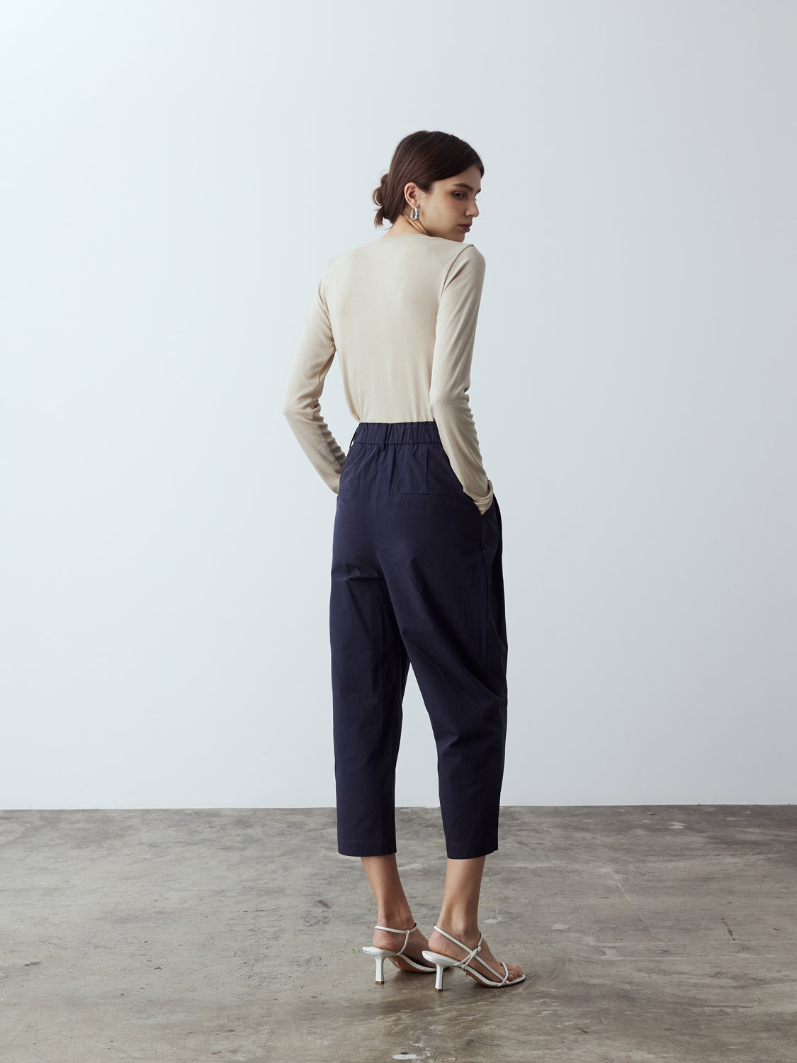 navy : Model is wearing the Cotton Tailored Trousers in Navy, which comes high-waisted with slash pockets at the sides, a concealed zip-fly closure and pleated details. Worn with the Fitted Long Sleeve T-Shirt in Sand and white strappy heels.