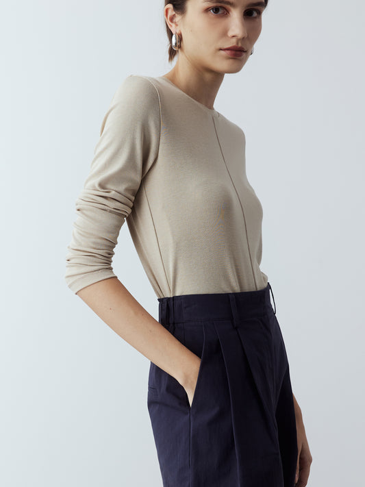 Model is wearing the Cotton Tailored Trousers in Navy, which comes high-waisted with slash pockets at the sides, a concealed zip-fly closure and pleated details. Worn with the Fitted Long Sleeve T-Shirt in Sand and white strappy heels.