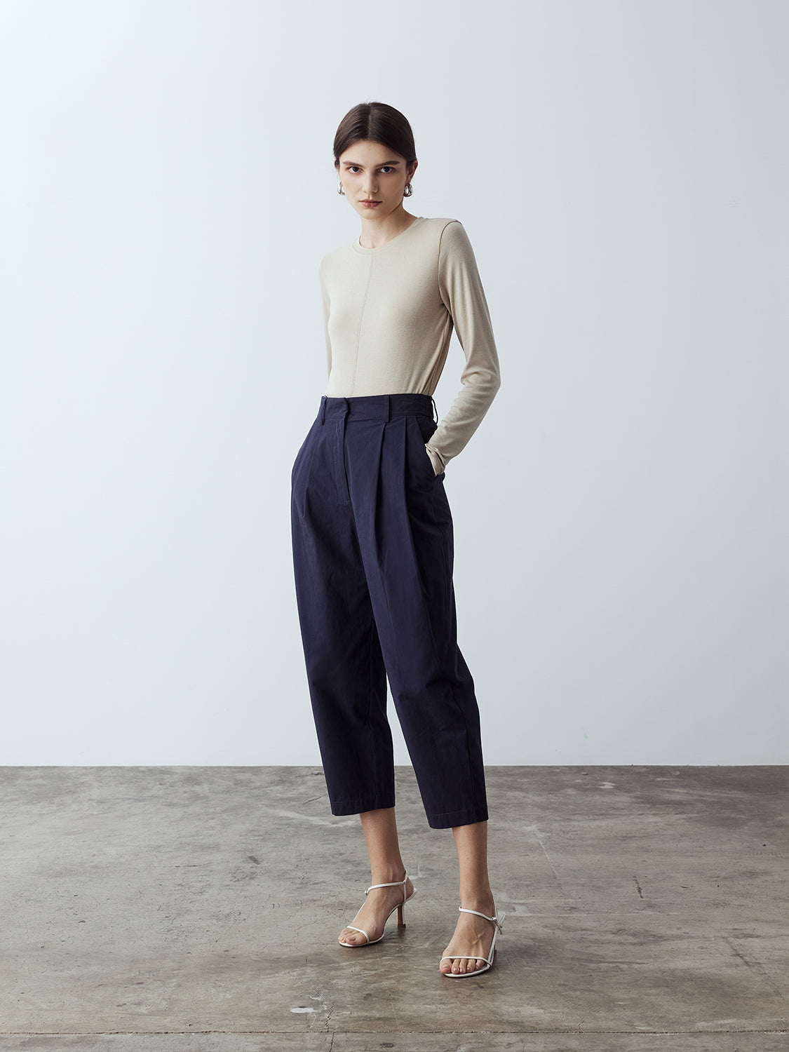 navy : Model is wearing the Cotton Tailored Trousers in Navy, which comes high-waisted with slash pockets at the sides, a concealed zip-fly closure and pleated details. Worn with the Fitted Long Sleeve T-Shirt in Sand and white strappy heels.