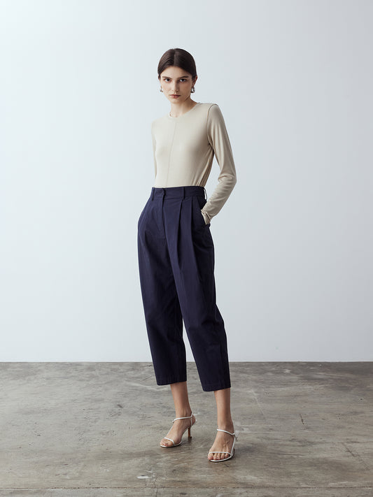Model is wearing the Cotton Tailored Trousers in Navy, which comes high-waisted with slash pockets at the sides, a concealed zip-fly closure and pleated details. Worn with the Fitted Long Sleeve T-Shirt in Sand and white strappy heels.