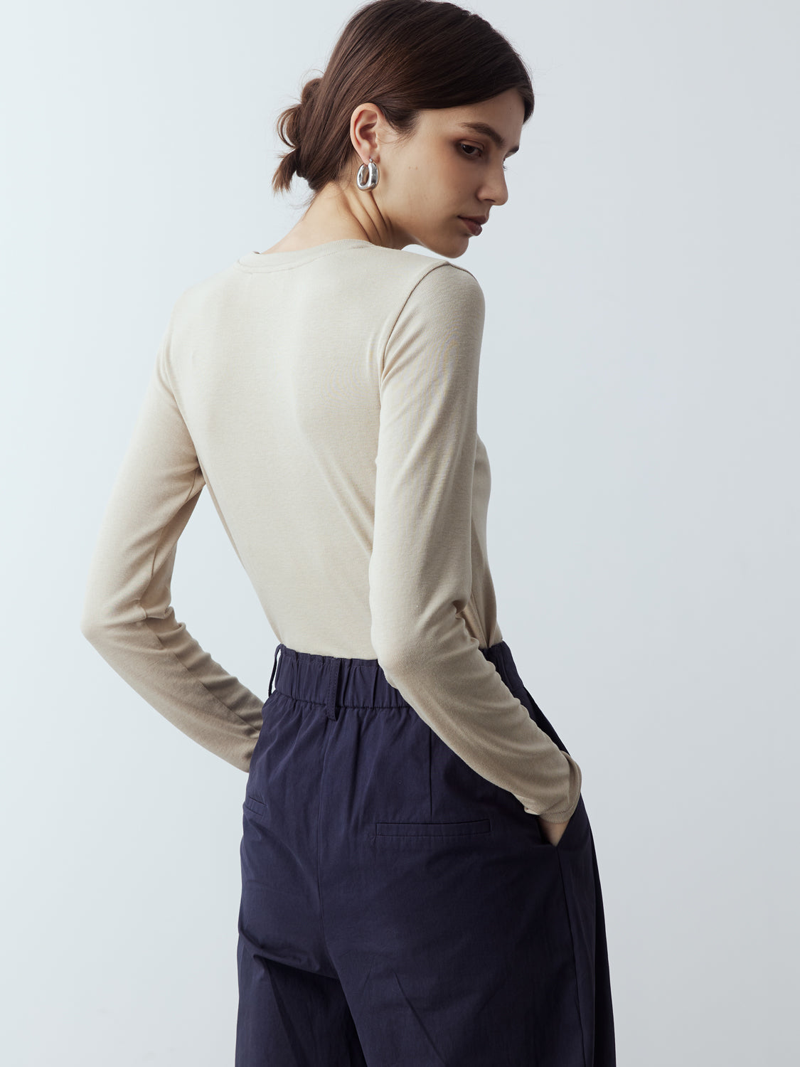 sand : Model is wearing the Fitted Long Sleeve T-Shirt in Sand, which comes with a rounded crew neckline and a centre front stitch line. Arm-hugging but gives a relaxed bodice. Worn with Cotton Tailored Trousers in Navy.