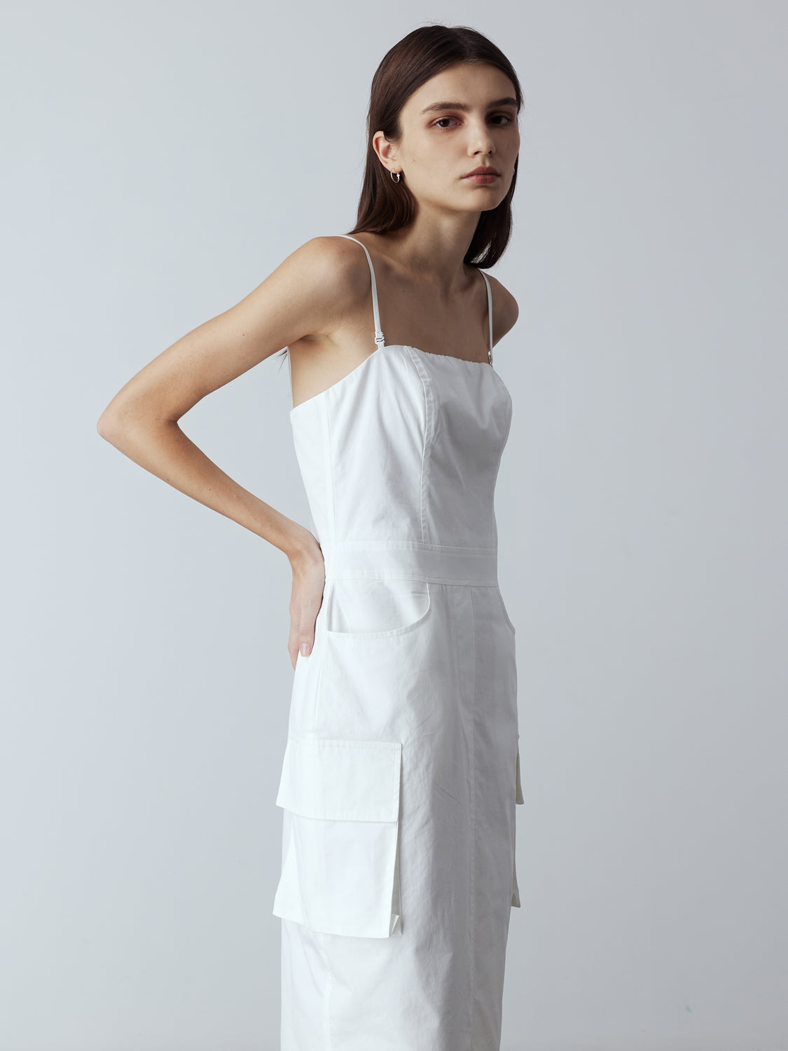white : Model is wearing the Adjustable Cargo Dress in White, which comes with back pockets, and cargo and slash pockets at the sides. This is a sleeveless garment with spaghetti straps. Can also be worn as a tube dress. Worn with silver heels.