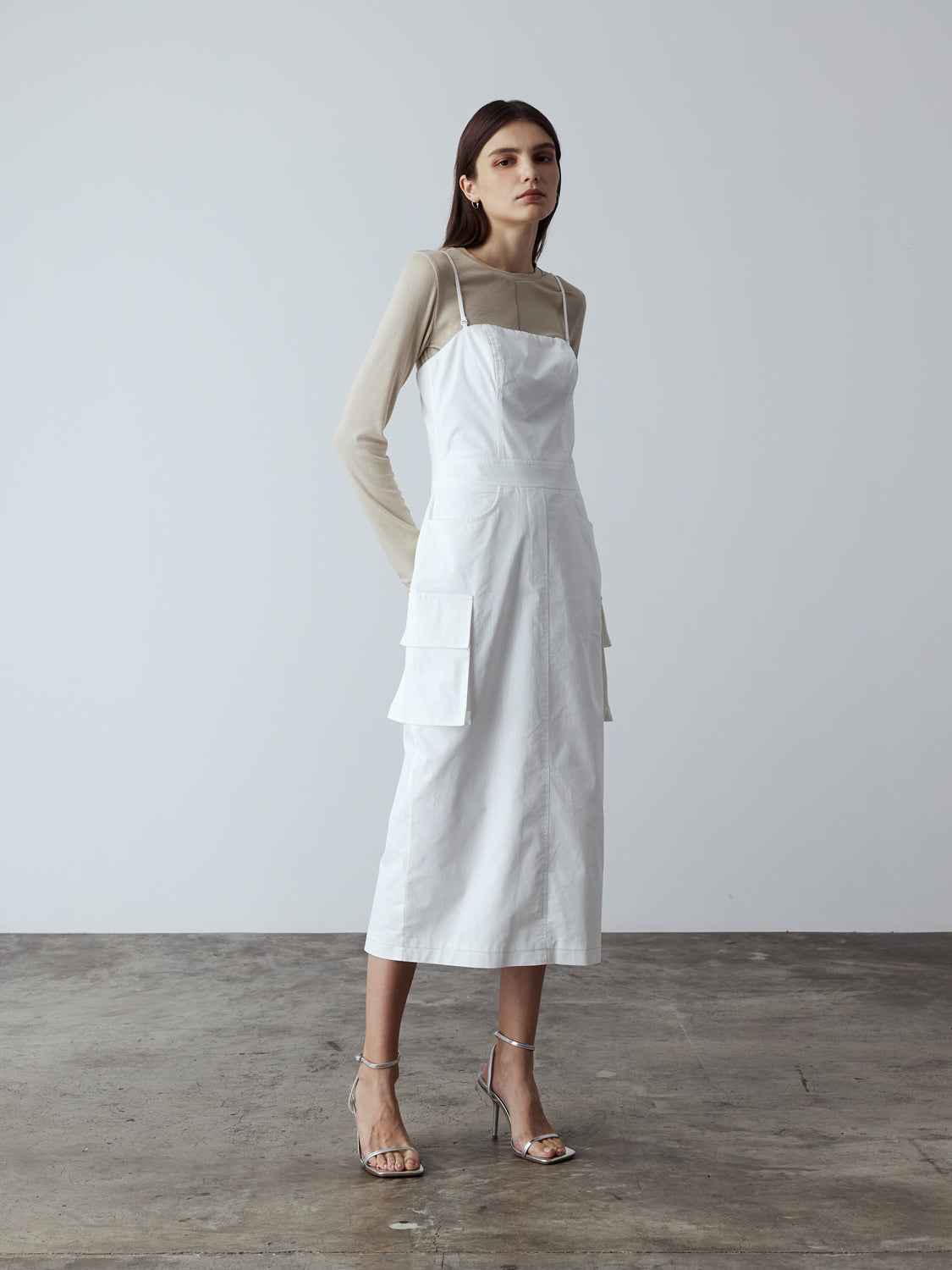 white : Model is wearing the Adjustable Cargo Dress in White, which comes with back pockets, and cargo and slash pockets at the sides. This is a sleeveless garment with spaghetti straps. Can also be worn as a tube dress. Worn with silver heels.